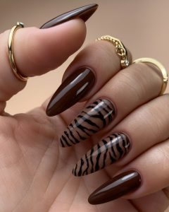 Mão com unhas pintadas em tons castanhos chocolate, com detalhes de linhas nail artist